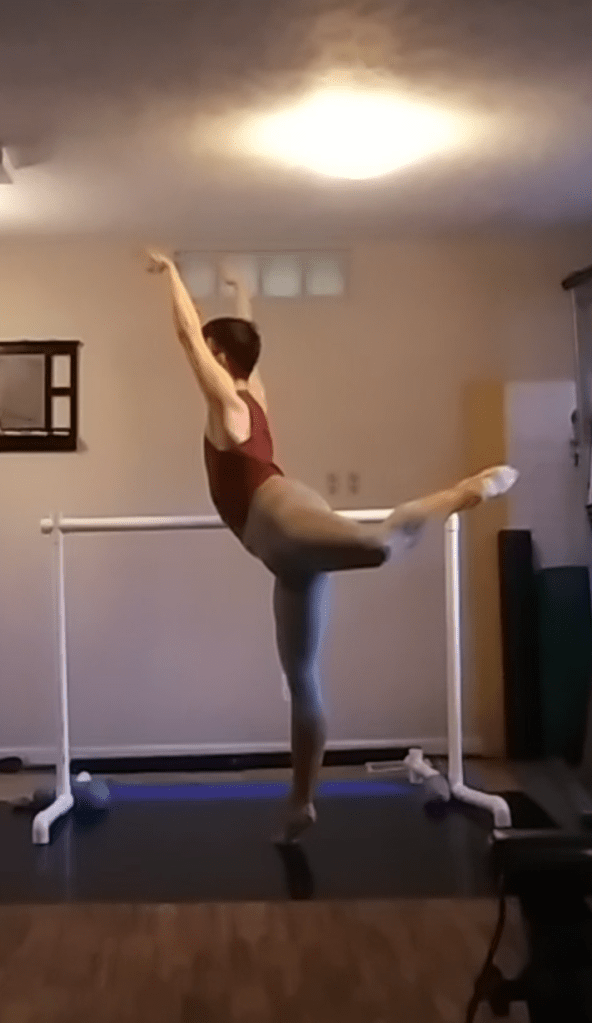 The author in an attitude balance on the ball of the right foot with the left leg, slightly bent, raised to hip level and both arms up.